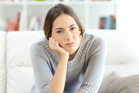 Front view portrait of a bored housewife looking at you sitting on a sofa at homeの写真素材