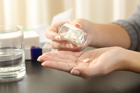 Close up of a woman taking a pill from bottle on a tableの写真素材