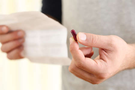 Close up of a man hands holding a pill and reading leaflet