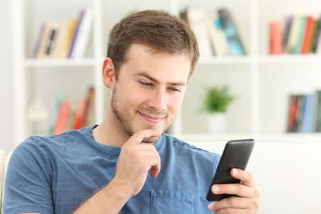 Man dating on line with a smart phone sitting on a sofa at homeの写真素材