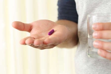 Close up of a man hand palm holding a capsule and a glass of water