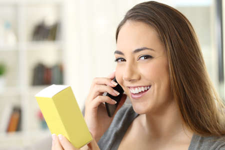 Girl calling on phone asking information about a medical product and looking at camera sitting on a couch in a house interiorの写真素材