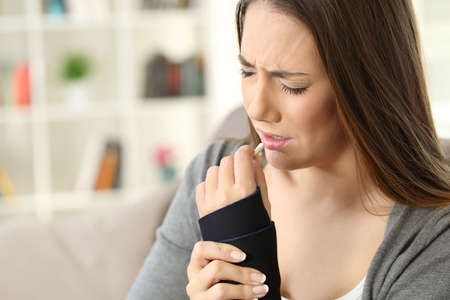Injured woman complaining taking a pill sitting on a couch in the living room in a house interior