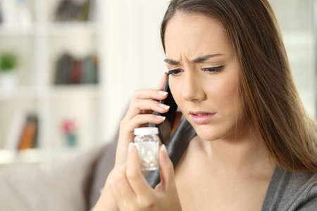 Worried girl asking information about medicines sitting on a couch in the living room in a house interiorの写真素材