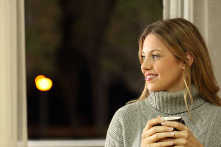 Portrait of a pensive woman looking at side holding a cup of coffee at home in the nightの写真素材