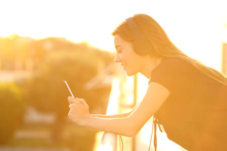 Side view portrait of a girl using a smart phone in a balcony at sunsetの写真素材