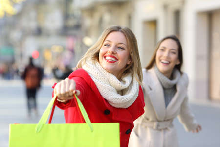 Two happy shoppers running searching shops outdoor on the streetの写真素材
