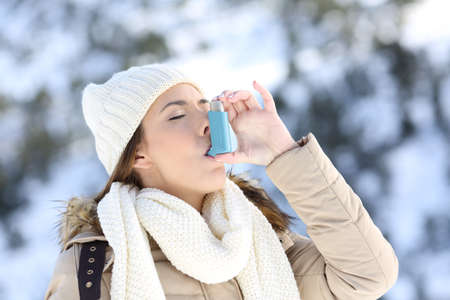 Portrait of a woman using an asthma inhaler in a cold winter with a snowy mountain in the backgroundの写真素材