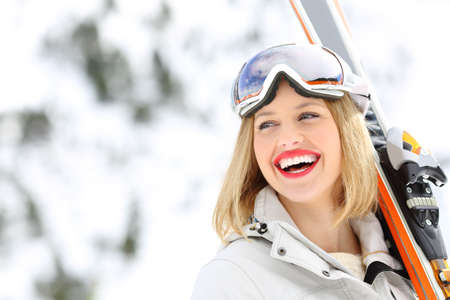 Portrait of a happy skier holding skis looking at side with a snowy mountain in the backgroundの写真素材