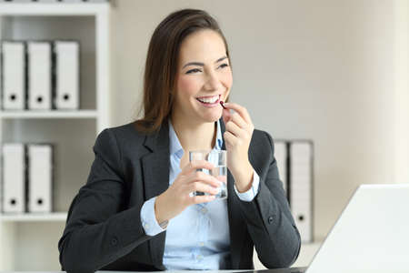 Happy businesswoman taking a pill working at officeの写真素材