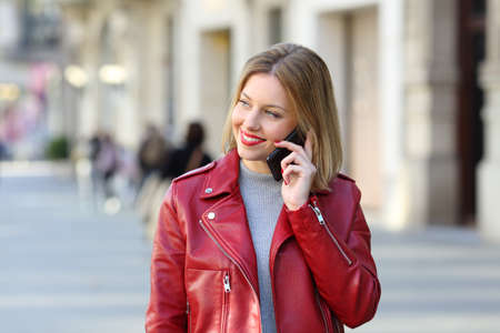 Front view portrait of a fashion blonde calling on phone and looking at side walking towards camera on the streetの写真素材