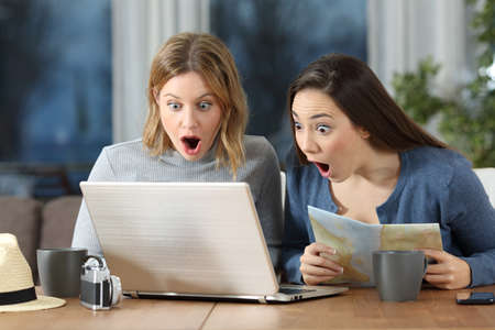 Two amazed tourists finding offers on line during a travel in an apartment in the eveningの写真素材