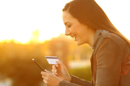 Side view portrait of a smiley girl buying on line with credit card and smart phone in a balcony at...