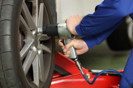 Close up of a car mechanic hands loosen wheel nuts with a pneumatic gun in a mechanical workshopの写真素材