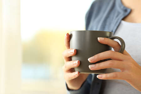 Close up of a woman hands holding a coffee mug standing at homeの写真素材
