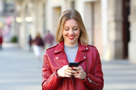 Front view portrait of a fashion blonde walking on the street and using a smart phoneの写真素材