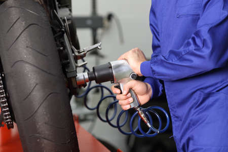 Close up of a motorcycle mechanic hands working usinb a pneumatic gun to thighten a nut in a mechanical workshopの写真素材