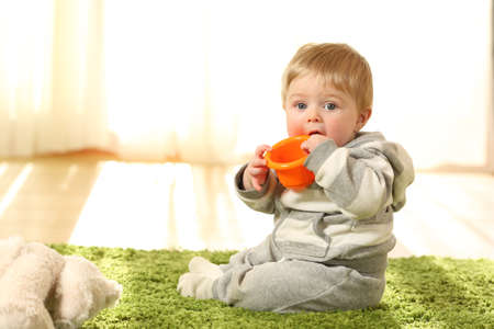 Portrait of a distracted baby biting a toy sitting on the floor at home