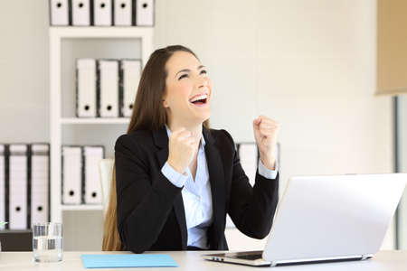 Excited businesswoman looking above celebrating success at officeの写真素材