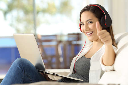 Satisfied woman wearing headphones relaxing listening to music looking at you sitting on a couch in the living room at homeの写真素材