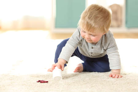 Baby in danger playing with a bottle of pills on the floor at homeの写真素材
