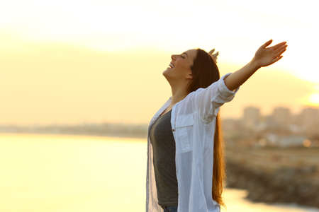 Side view portrait of a woman breathing deep fresh air outstretching arms at sunset with the city in the backgroundの写真素材