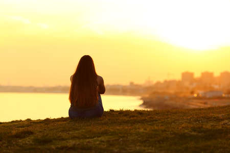 Back view backlight portrait of a single woman watching a sunset on the city with a warm light in the backgroundの写真素材