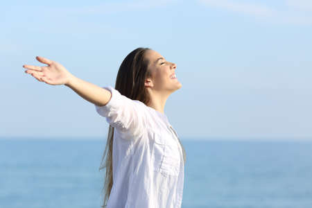 Side view portrait of a happy girl breathing fresh air on the beach outstretching armsの写真素材