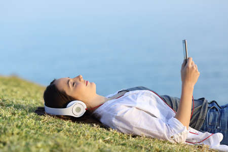 Side view portrait of a woman relaxing listening to music lying on the grass with the sea in the backgroundの写真素材