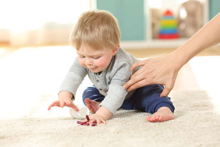 Mother hand preventing the baby from eating pills on the flor at homeの写真素材