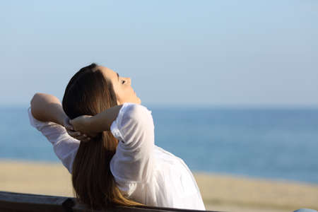 Woman relaxing sitting on a bench on the beach with the sea in the backgroundの写真素材