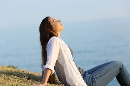 Side view portrait of a relaxed woman breathing fresh air sitting on the grass with the sea and sky in the backgroundの写真素材