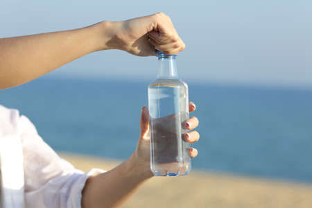 Close up of a woman hands opening a bottle of water outdoors on the beachの写真素材