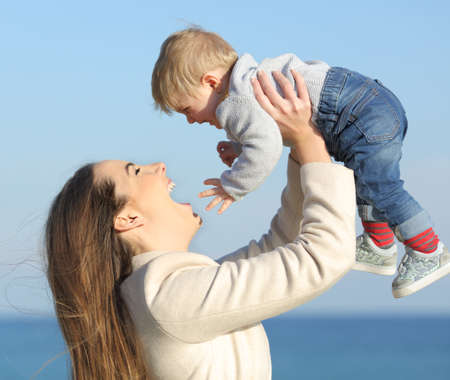 Side view portrait of a happy mother raising her baby son outdoors on the beachの写真素材