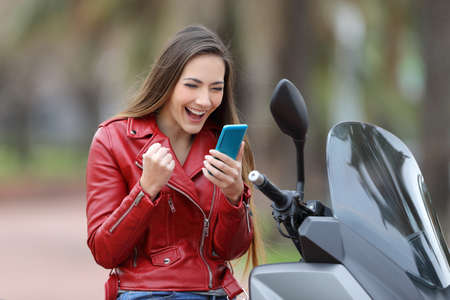 Excited motorbiker on a motorcycle reading good news online in a smart phoneの写真素材