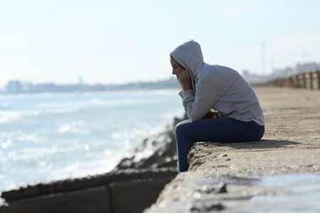 Side view portrait of a sad teenager girl alone on the beachの写真素材