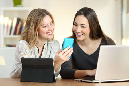 Two happy girls checking information in multiple devices at homeの写真素材