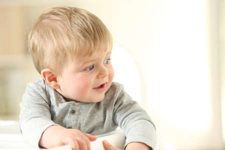 Portrait of a happy kid looking at side sitting on a high chair at homeの写真素材