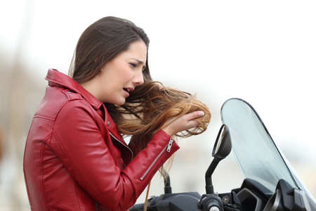 Portrait of a sad biker woman complaining about tangled hair after a motorkike travel
