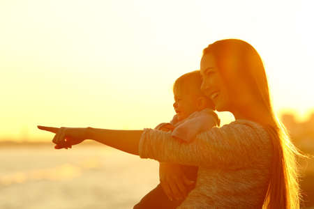Happy mother and kid son looking away and pointing horizon at sunsetの写真素材