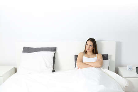 Front wide angle view portrait of an angry woman sitting on the bed looking at side with an isolated white space aboveの写真素材