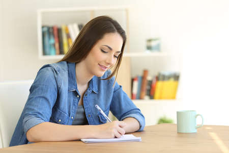 Relaxed girl writing in a notebook on a table at homeの写真素材