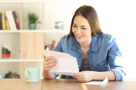 Happy woman reading a letter on a table at homeの写真素材