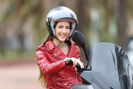 Happy biker wearing an helmet sitting on her motorbike looking at camera on the street