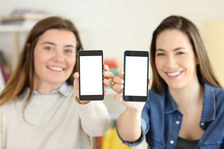 Two happy students showing their both smart phone screens to camera at homeの写真素材