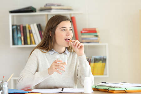 Student taking a pill to relief illness symptoms while is studying at home