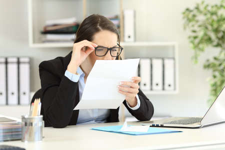 Office employee wearing eyeglasses with bad graduation having eyesight problems reading a letterの写真素材