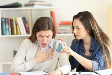 Student helping to her asmathic friend giving the inhaler during an asthma attackの写真素材