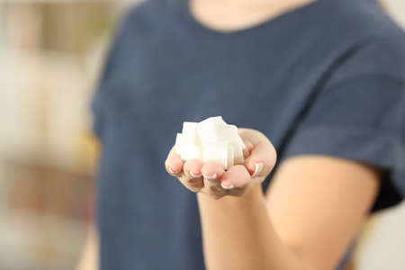 Closeup of a woman hand holding sugar cubes to camera at homeの写真素材