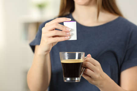 Front view close up of a woman hands throwing saccharin into a coffee cup at homeの写真素材